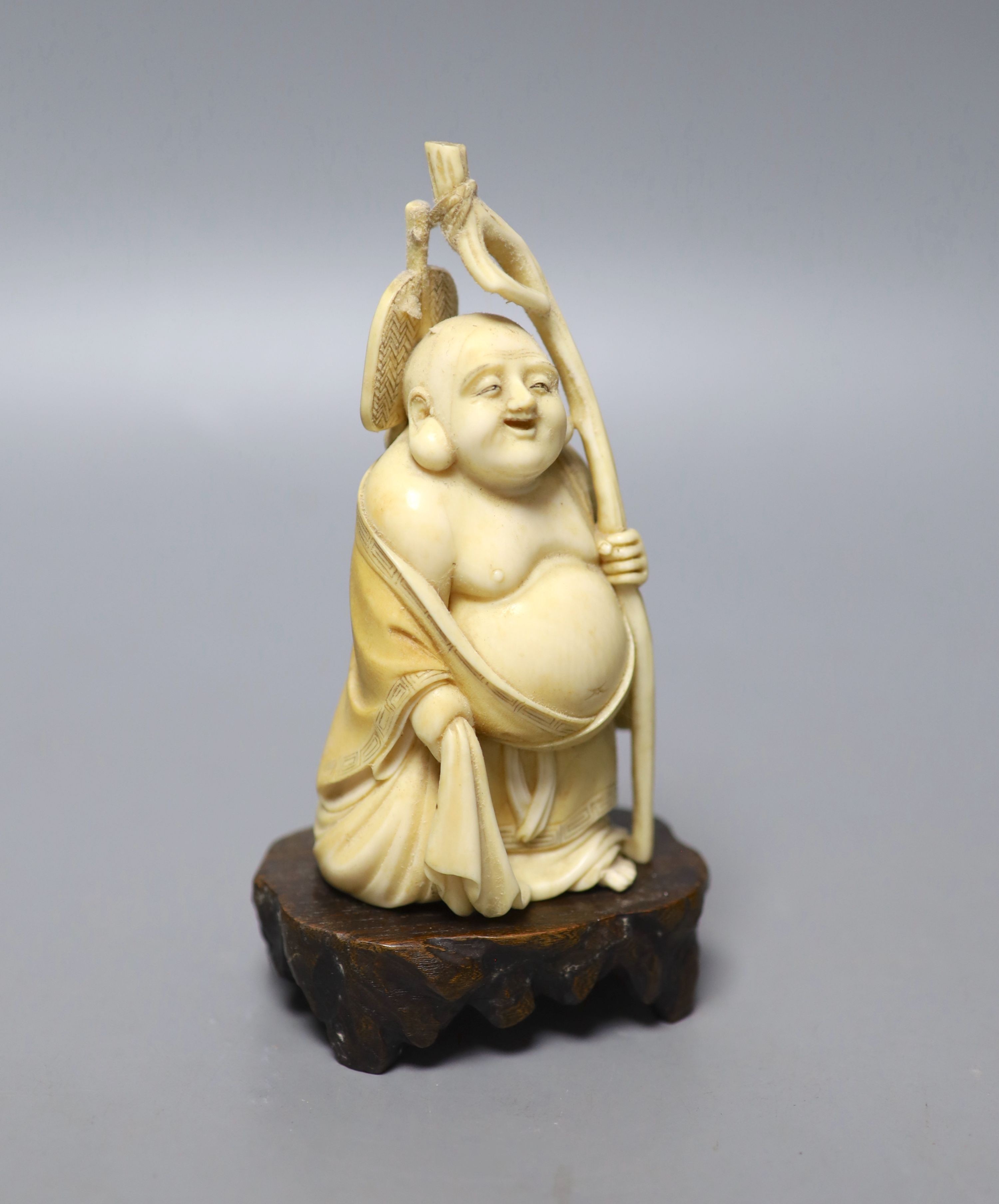 An early 20th century Japanese carved ivory okimono of Hotei, and wood stand, 15cm